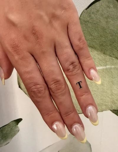 tatouage calligraphique minimaliste lettre T sur le doigt d'une femme - Tattoo chez L