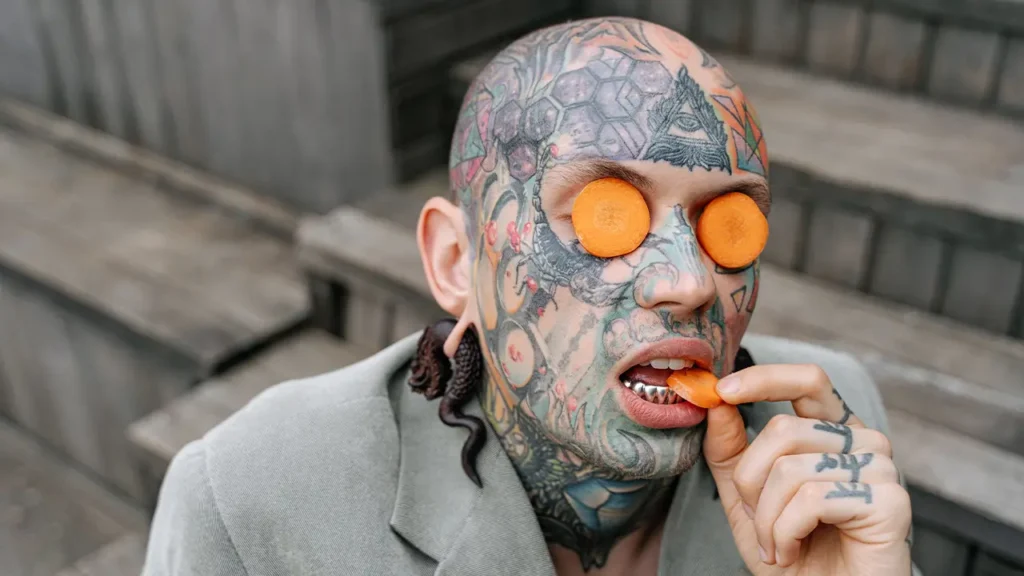 un homme tatoué mange des carottes