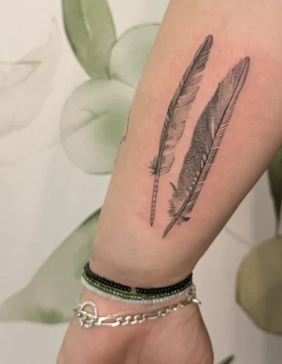 tatouage de deux plumes en style semi-réalisme sur le côté de l'avant-bras d'une femme